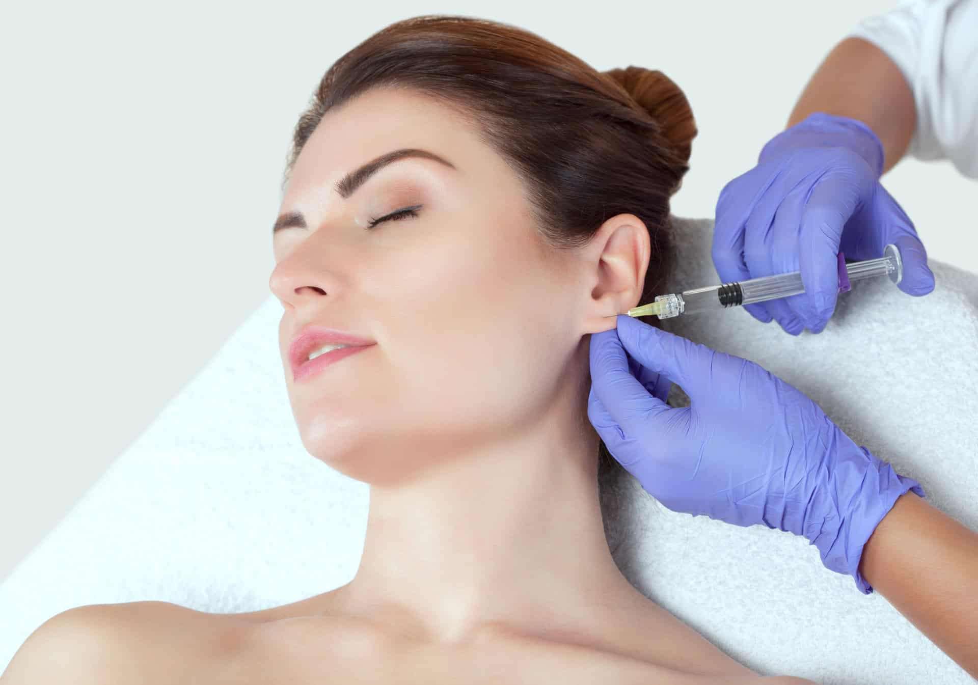 The doctor cosmetologist makes the injections procedure for smoothing wrinkles and against flabbiness of the skin on earlobe of a beautiful, young woman in a beauty salon. The doctor cosmetologist makes the injections procedure for smoothing wrinkles and against flabbiness of the skin on earlobe of a beautiful, young woman in a beauty salon.